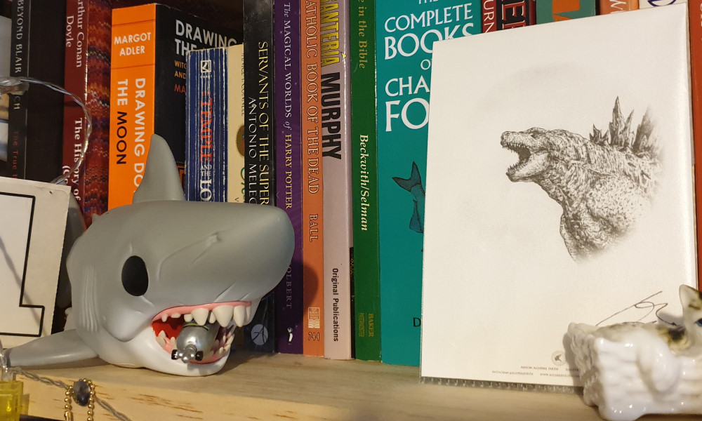 A bookshelf with a Funko Pop of Jaws next to a drawing of Godzilla