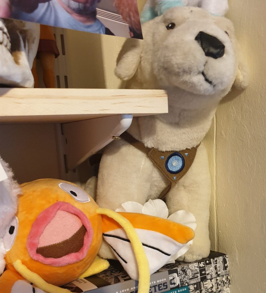 A stuffed toy Naga and a stuffed toy Magikarp tucked between shelves