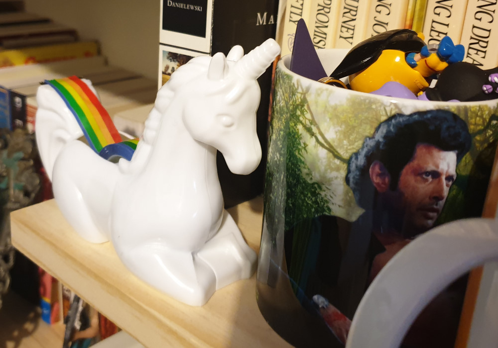 A tape dispenser in the shape of a unicorn and a mug filled with small keychains