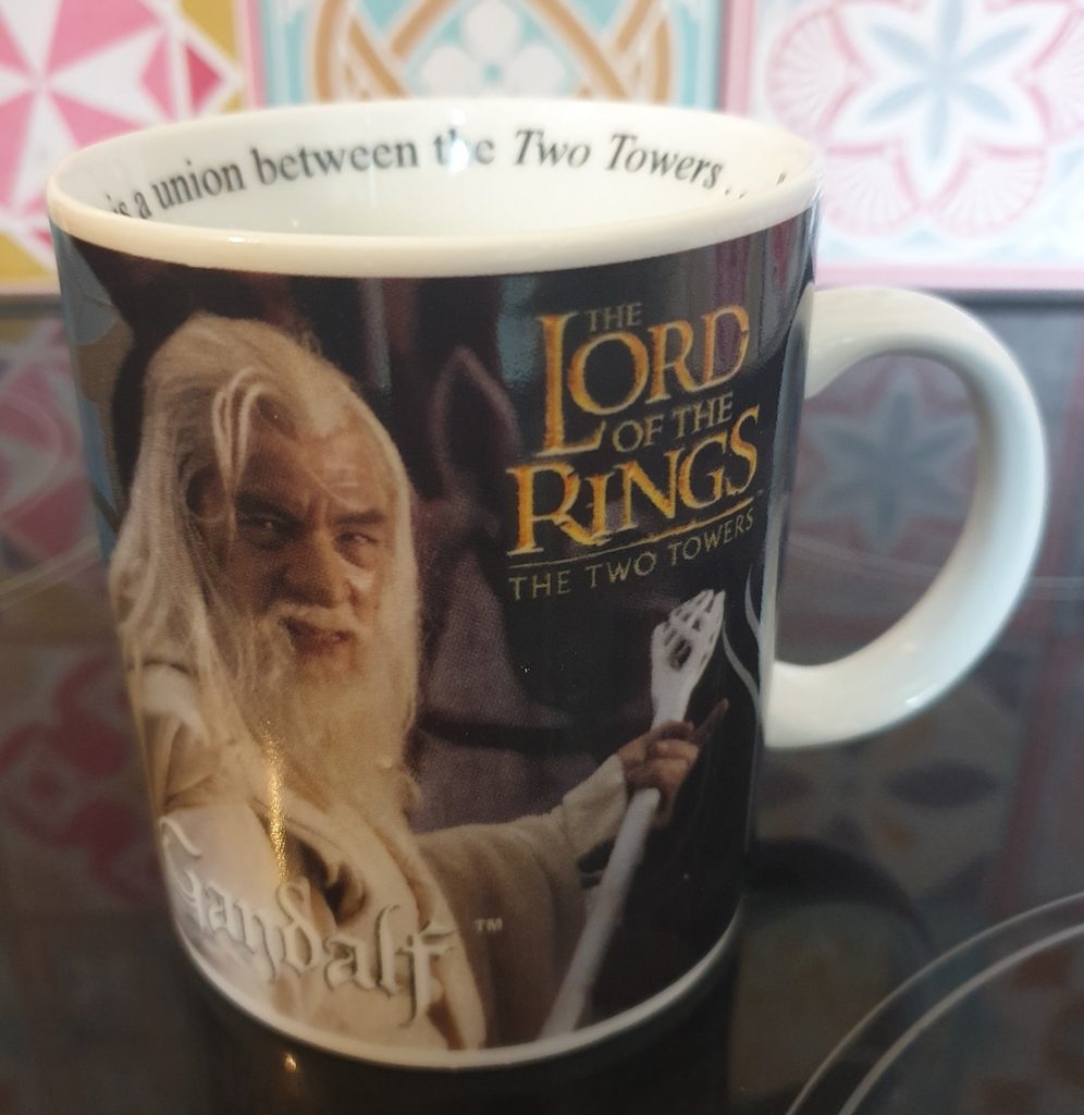 A coffee mug sitting on top of the stove, with a picture of Gandalf the White and the Lord of the Rings: The Two Towers logo on it.